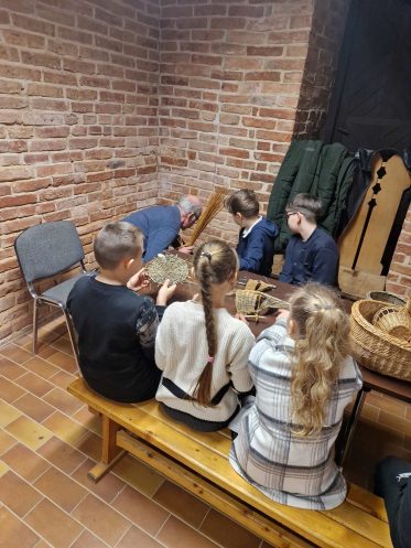 vaikai susėdę aplink stalą pina iš vytelių